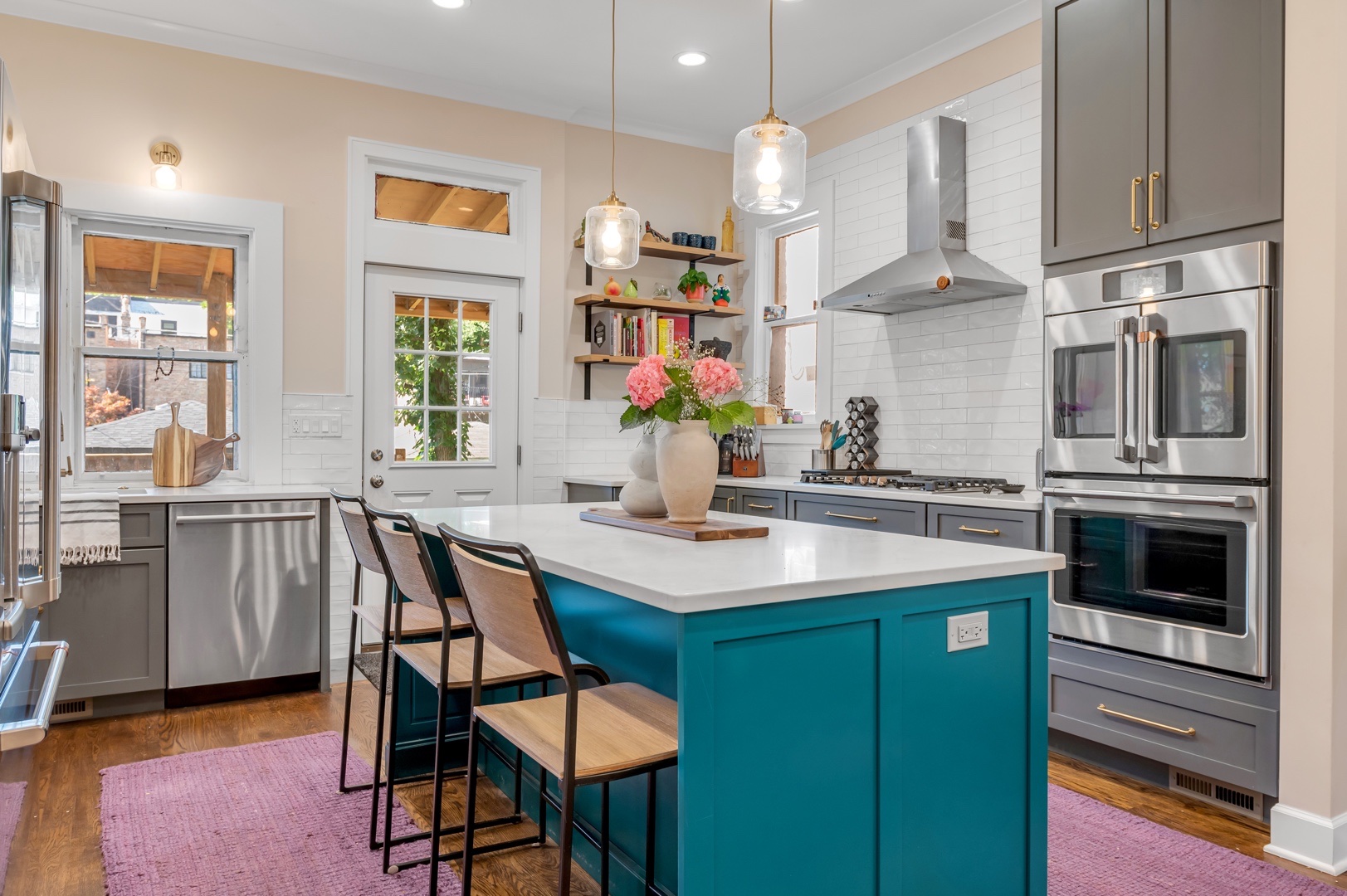 Kitchen remodel with two tone cabinets, white quartz countertop, wood floors, open shelving, brass hardware, stainless steel appliances, pendants, can lights, and subway tile